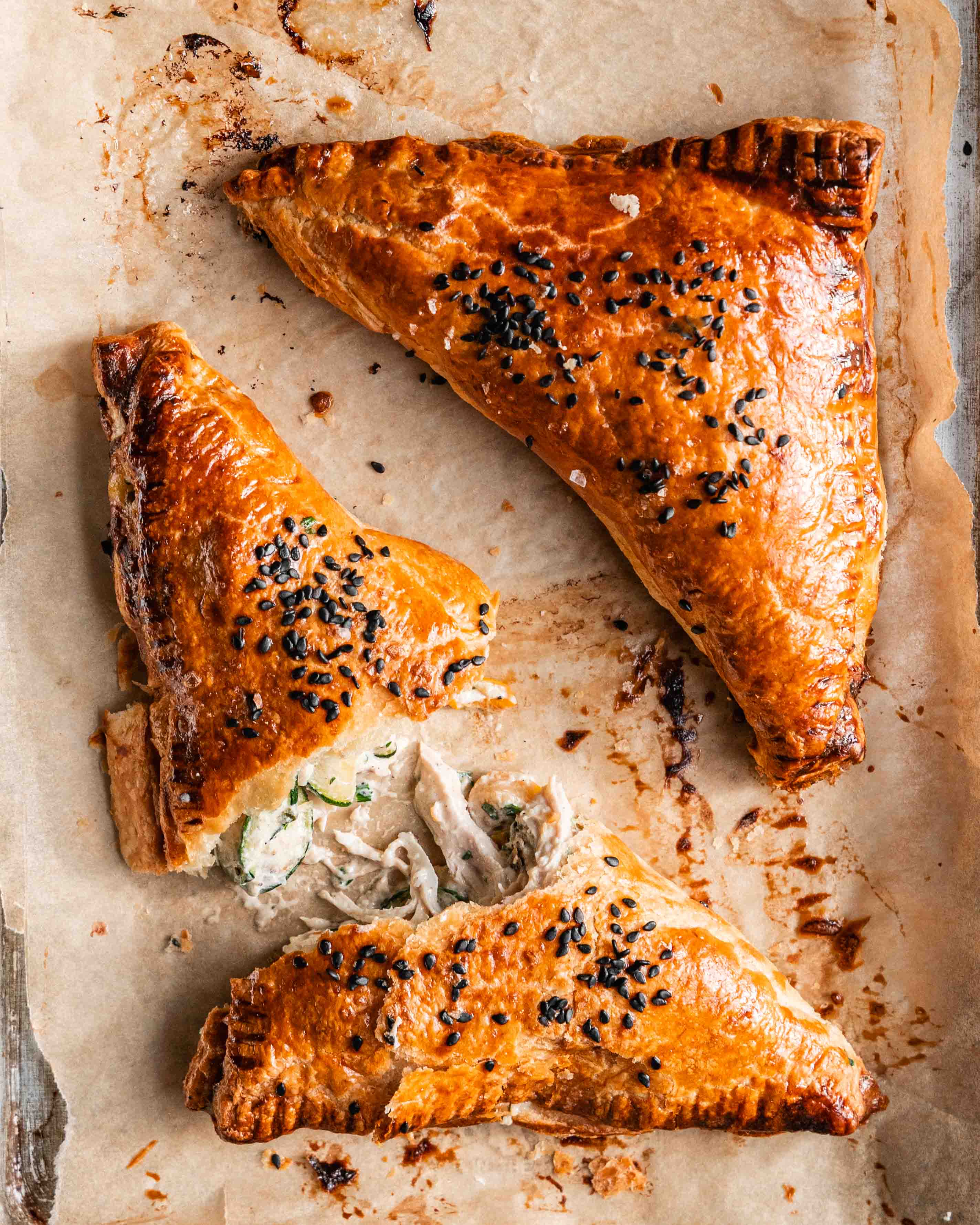 Chicken and jammy courgette pasties on a lined baking sheet. One pasty is broken in half.