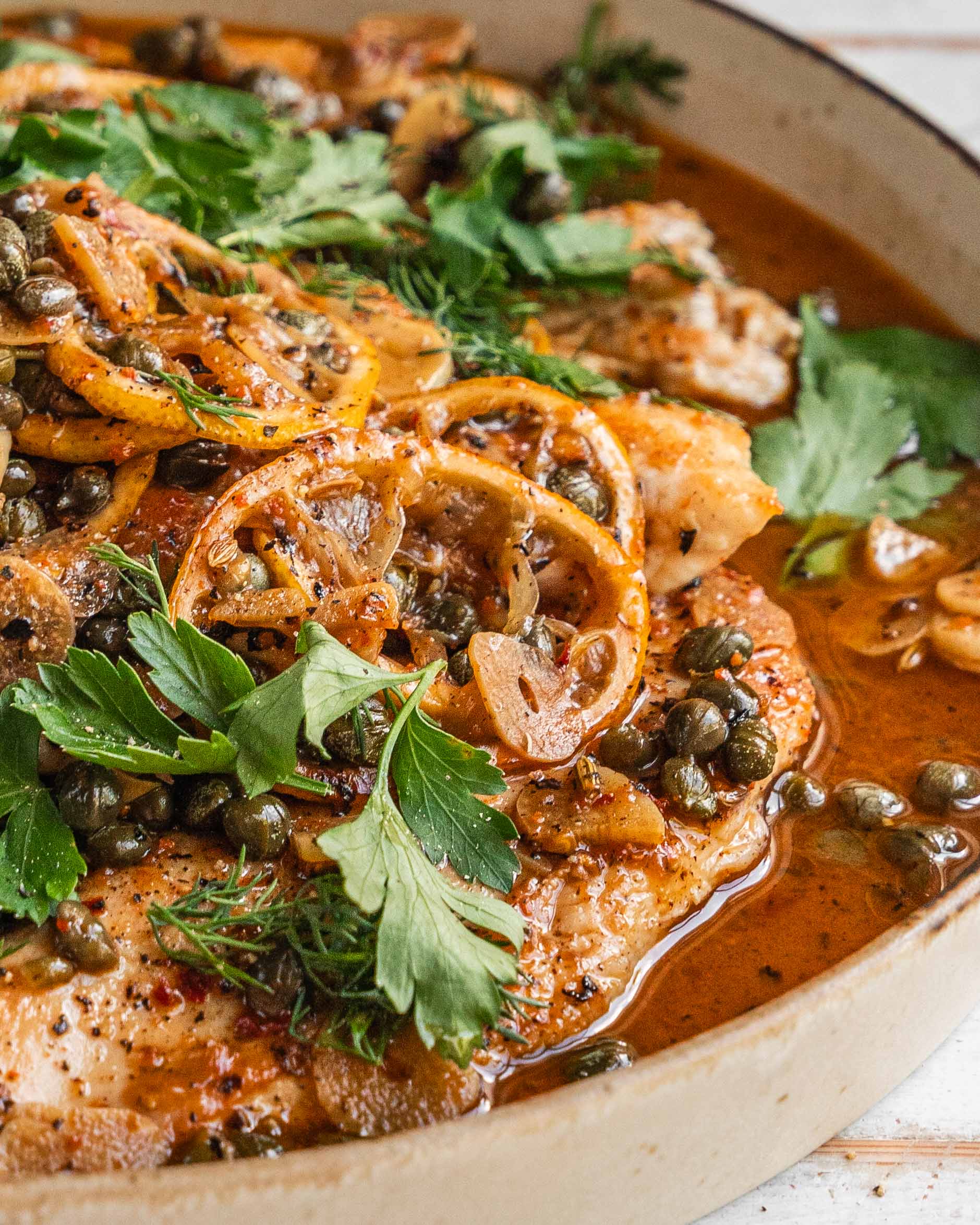 Closeup of spicy brown butter chicken piccata in a cream-coloured dish.