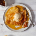 Overhead view of brown butter crepe suzette, topped with vanilla ice cream and orange segments, with golden orange sauce coating the plate
