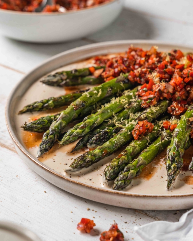 close up of asparagus with Turkish Ezme inspired Tomato Salad and Creamy Tahini Dressing on a white plate with a white wood background
