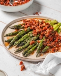 Asparagus with Turkish Ezme inspired Tomato Salad and Creamy Tahini Dressing on a white plate with a white wood background