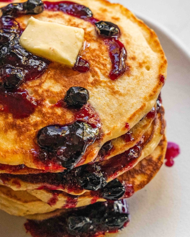 A close up of a stack of blueberry and polenta pancakes on a white plate